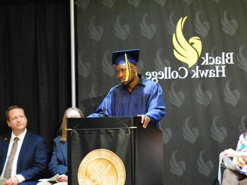 GED grad wearing cap & gown and speaking at podium on stage