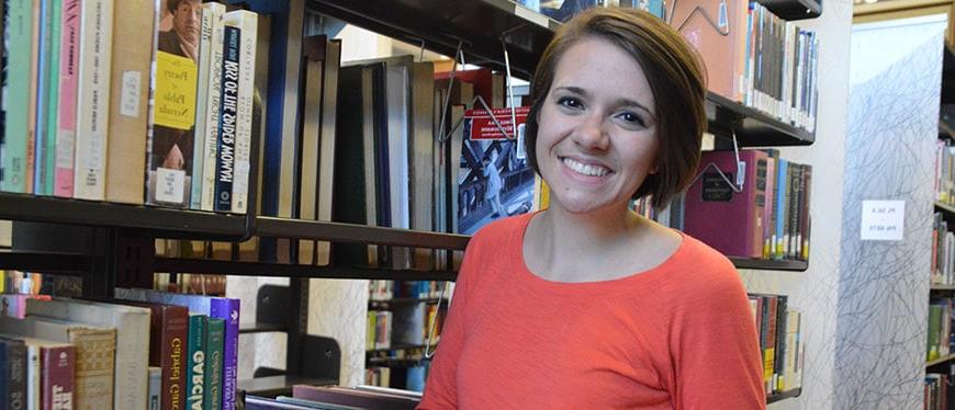 Woman in orange shirt standing in front of library book shelves