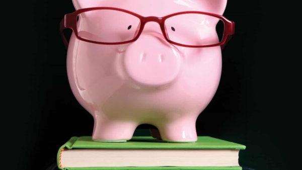 pink piggy bank wearing red glasses on stack of books