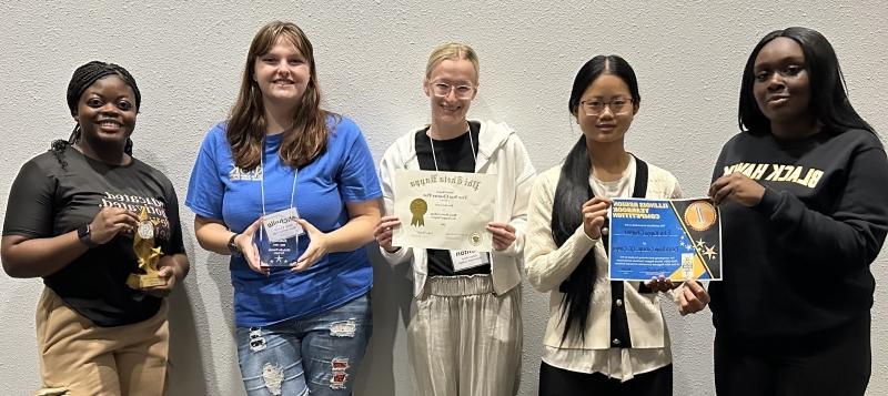 5 smiling students standing together holding awards and certificates